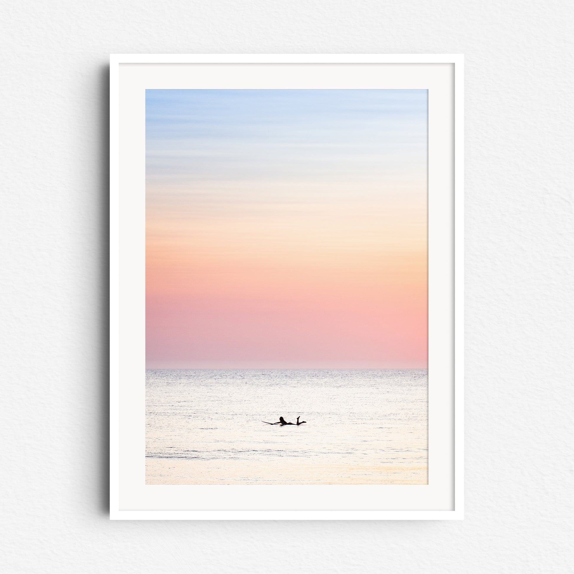 Warm summer surf in the North Sea with the silhouette of a female surfer visible, captured in pastel tones and framed in white wood for a fresh, light aesthetic.