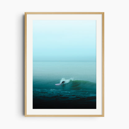 A lone The Hague surfer glides on turquoise waves with a pink longboard. Framed in natural wood for an organic touch.