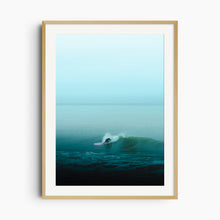 Load image into Gallery viewer, A lone The Hague surfer glides on turquoise waves with a pink longboard. Framed in natural wood for an organic touch.
