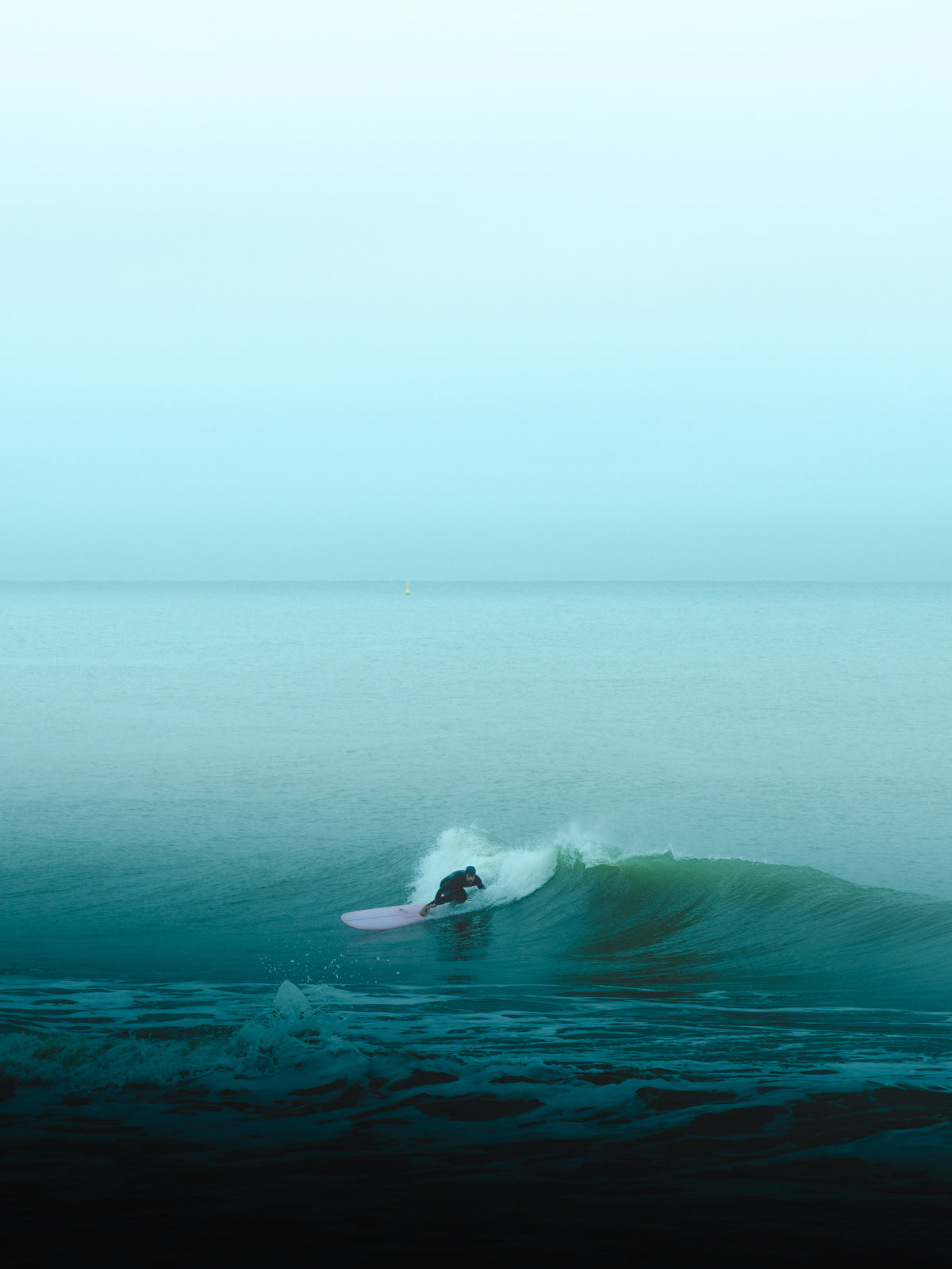 A surfer in The Netherlands surfs a wave on a pink surfboard in a moody turquoise surf scene.