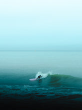 Load image into Gallery viewer, A surfer in The Netherlands surfs a wave on a pink surfboard in a moody turquoise surf scene.
