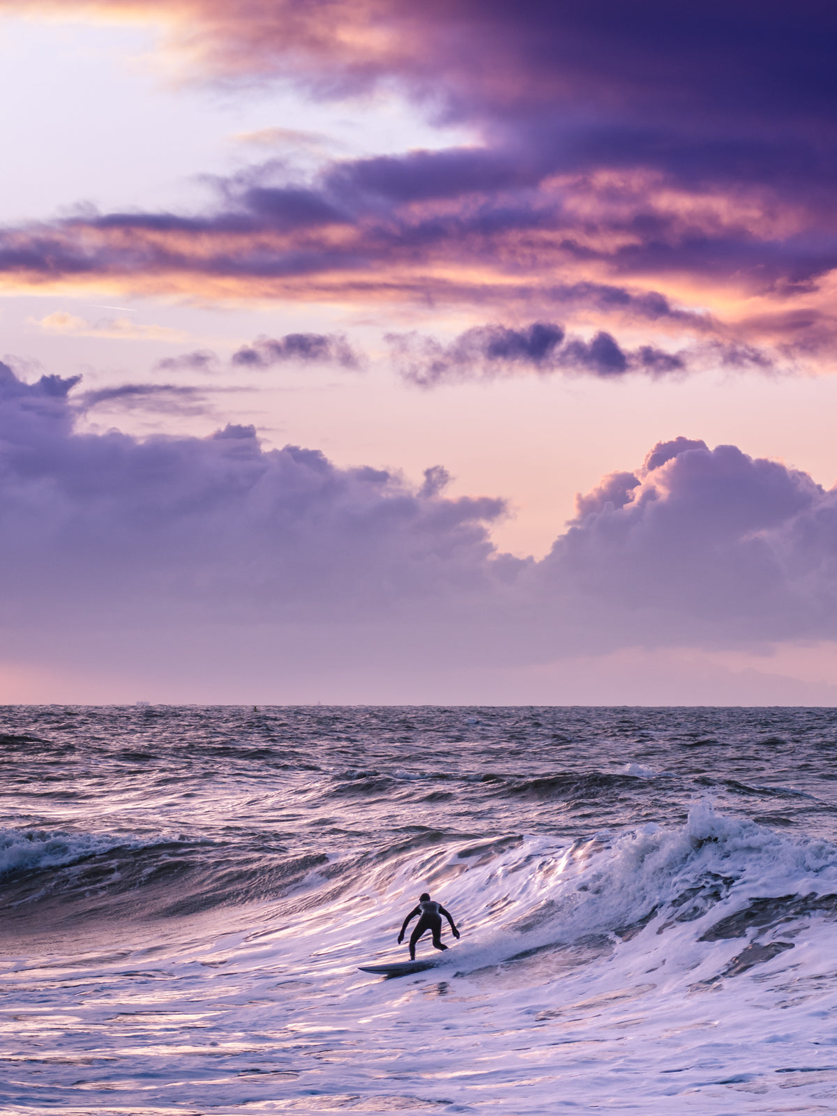 One surfer on a wave in The Netherlands with a bright purple sky and purple glow on the north sea surface. The Hague artwork.