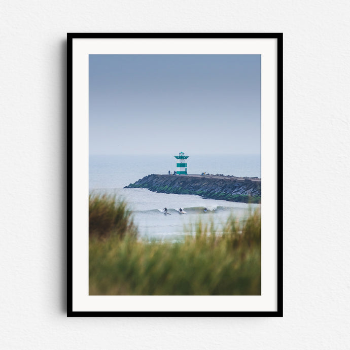 Scenic view of orange dune grass and Scheveningen harbor wall with surfers in the water, framed in black wood, ideal for poster Scheveningen lovers.