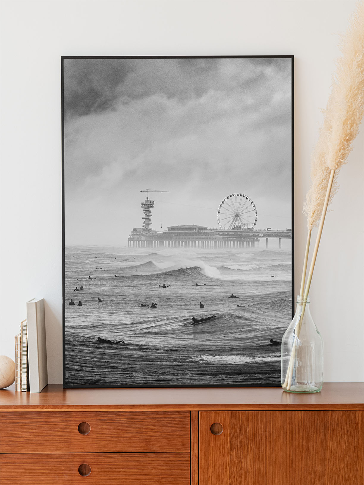 Top-selling photo of Scheveningen Pier with surfers in a thin aluminium frame standing on a wooden cabinet. Captured by Jop Hermans.