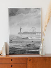 Load image into Gallery viewer, Top-selling photo of Scheveningen Pier with surfers in a thin aluminium frame standing on a wooden cabinet. Captured by Jop Hermans.
