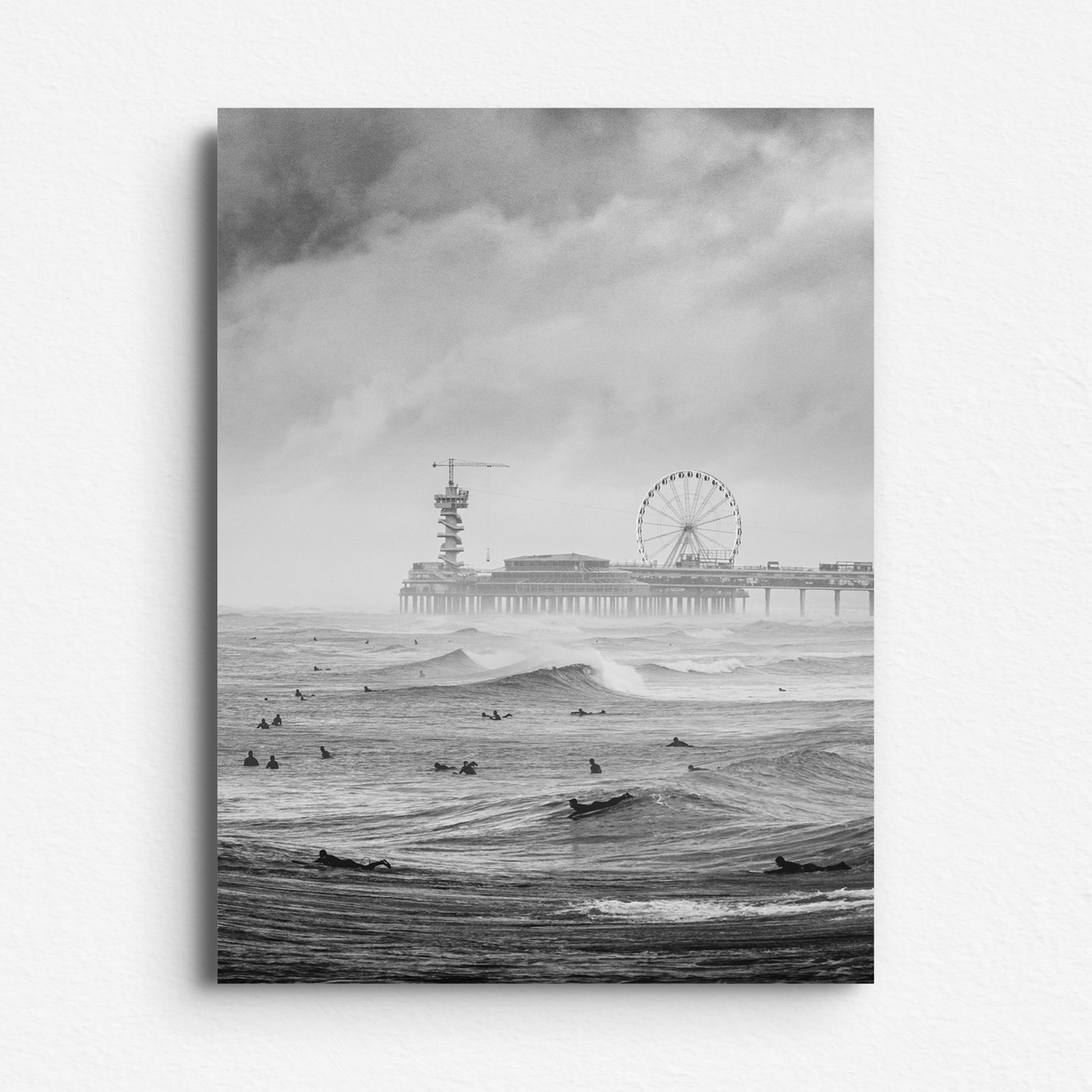 Scheveningen Pier with surfers in perfect waves, printed on Dibond for a sleek, modern finish. Moody black and white photography by Jop Hermans.