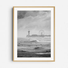 Load image into Gallery viewer, Classic Dutch surf scene in black and white. With surfers, the iconic Scheveningen pier and moody skies, framed in natural wood for a balanced, earthy display.
