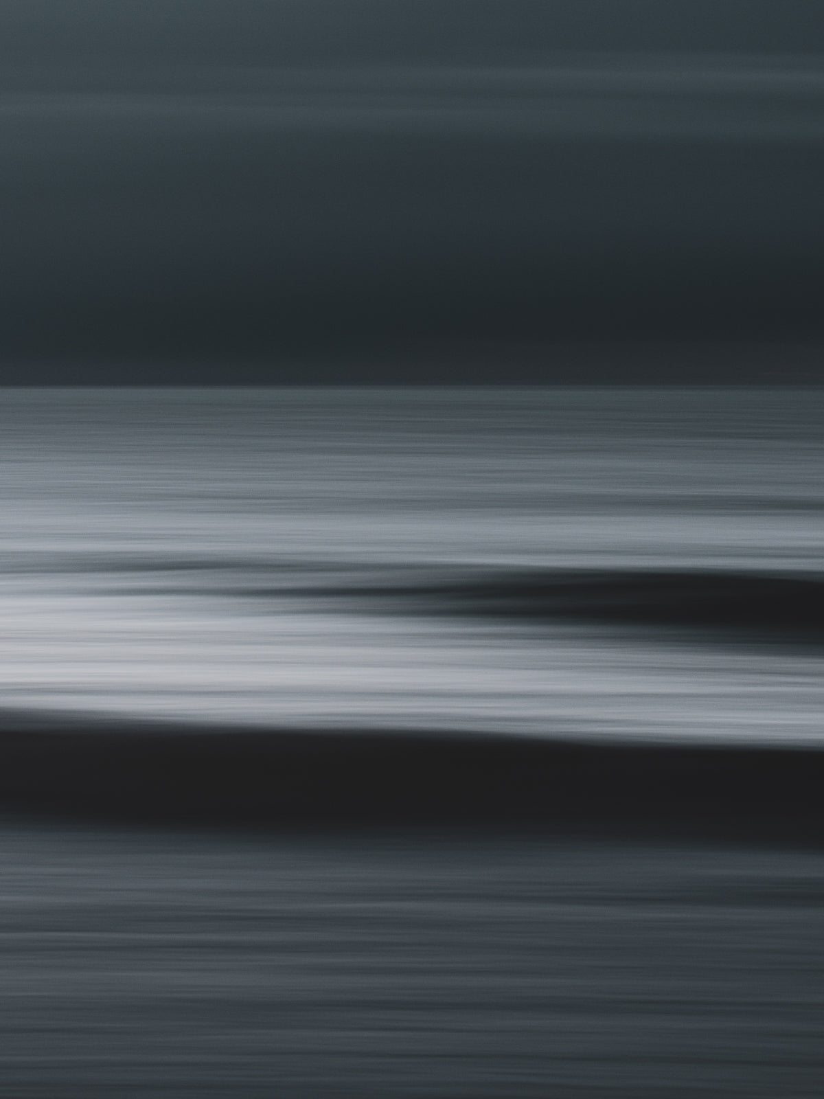 Abstract ocean view with two waves visible in a motion blur. Minimalist long-exposure photography with a dark mood.