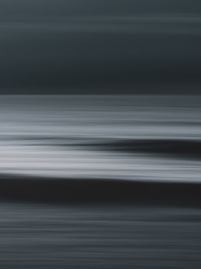 Abstract ocean view with two waves visible in a motion blur. Minimalist long-exposure photography with a dark mood.