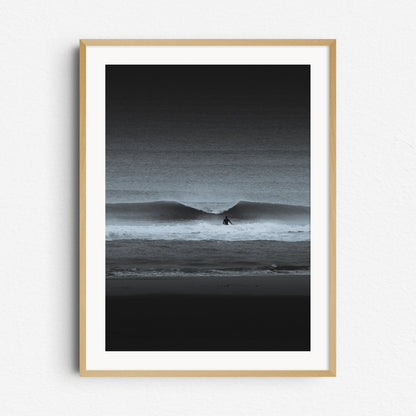 A moody black-and-white photo of a surfer entering the water. Framed in natural wood for a warm, organic touch.