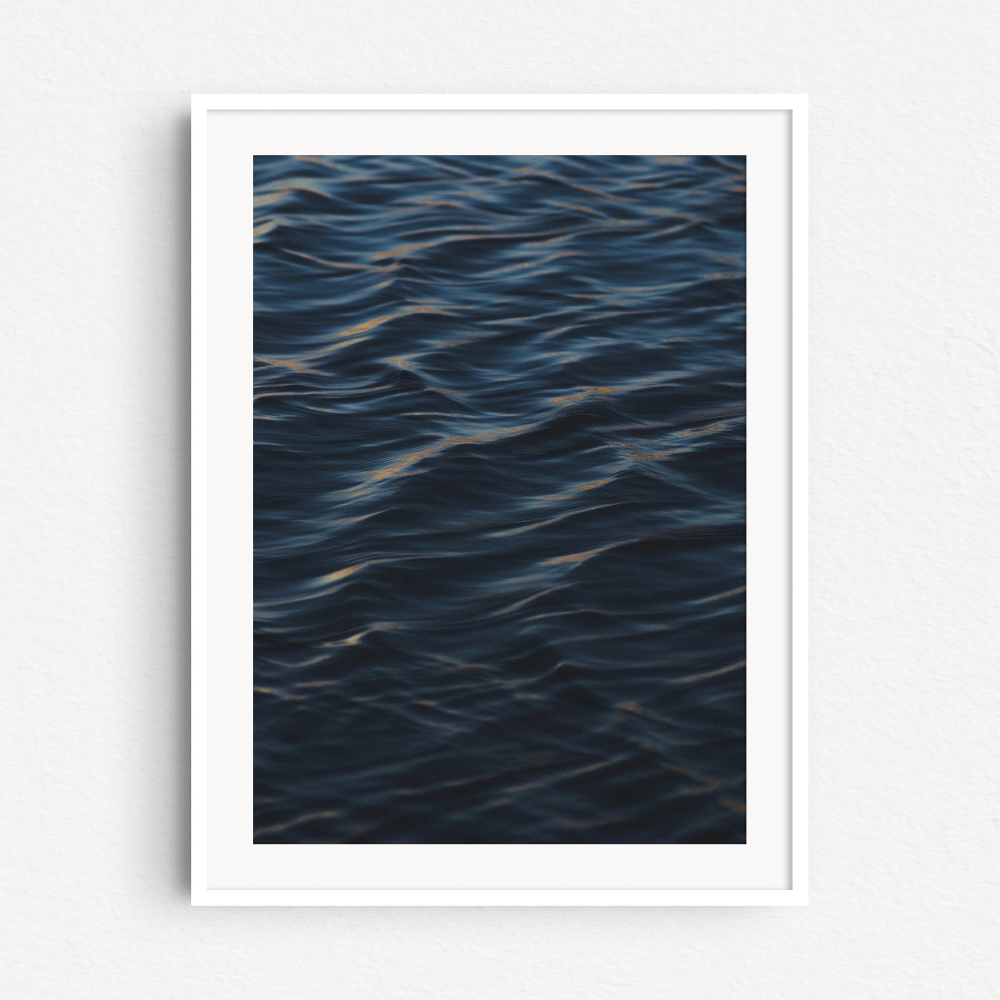 Surf photo art print from The Hague, showcasing a peaceful ocean wave. Print in a white wooden frame.
