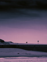 Load image into Gallery viewer, The silhouette of a surfer running across the beach carrying a surfboard. The sky is dark and has a purple glow.
