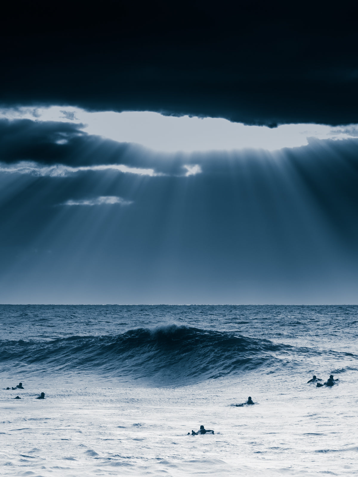 Dramatic surf landscape with sunlight through clouds, surfers, and deep blues. A striking North Sea photo for your wall.