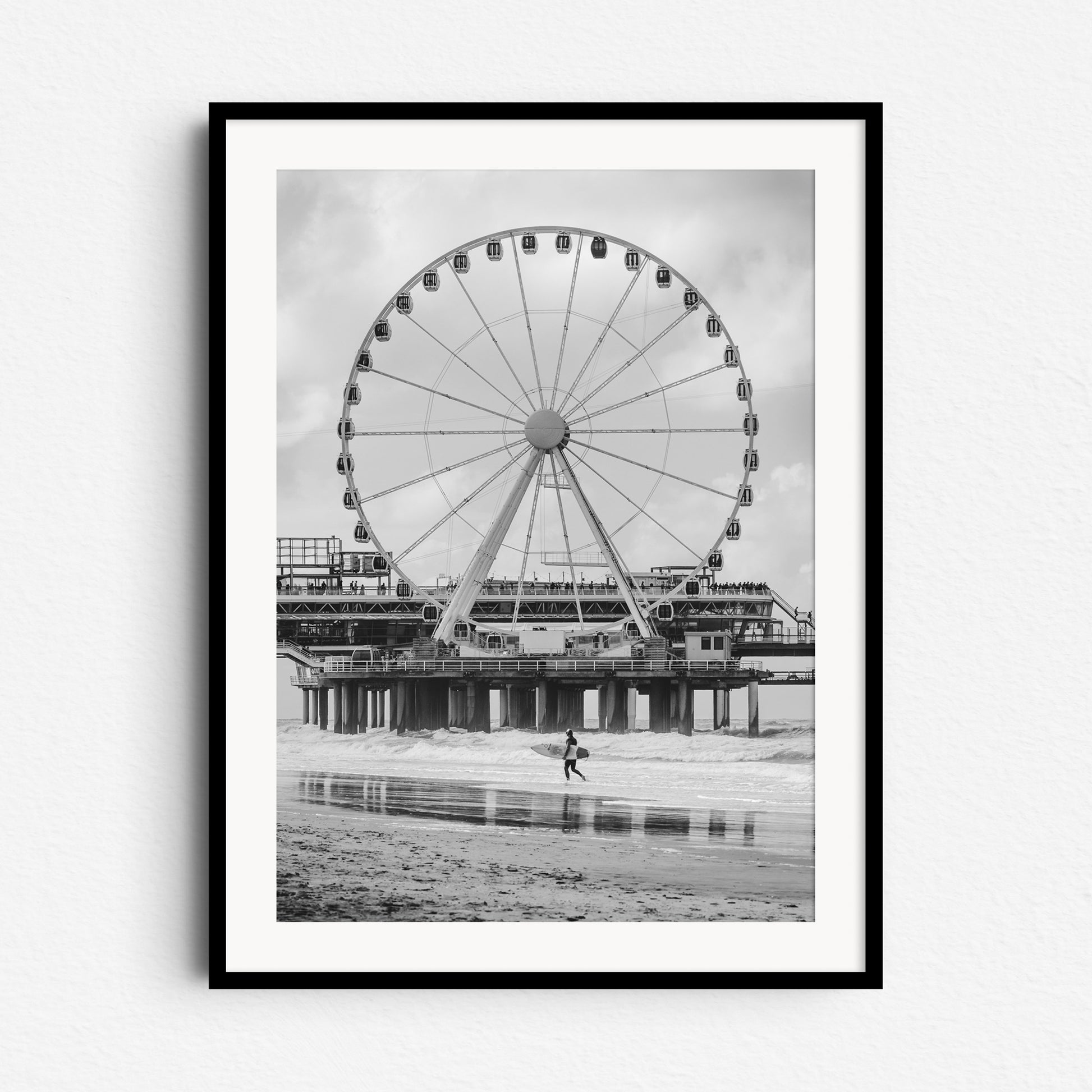 Scheveningen Pier’s ferris wheel with a surfer in front. Black and white North Sea surf photography from The Hague, framed in black wood for a bold and striking wall art piece.