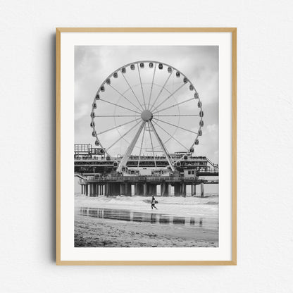 Surfer walks in front of the ferris wheel on Scheveningen Pier, framed in natural wood for a warm, classic display of this coastal scene.