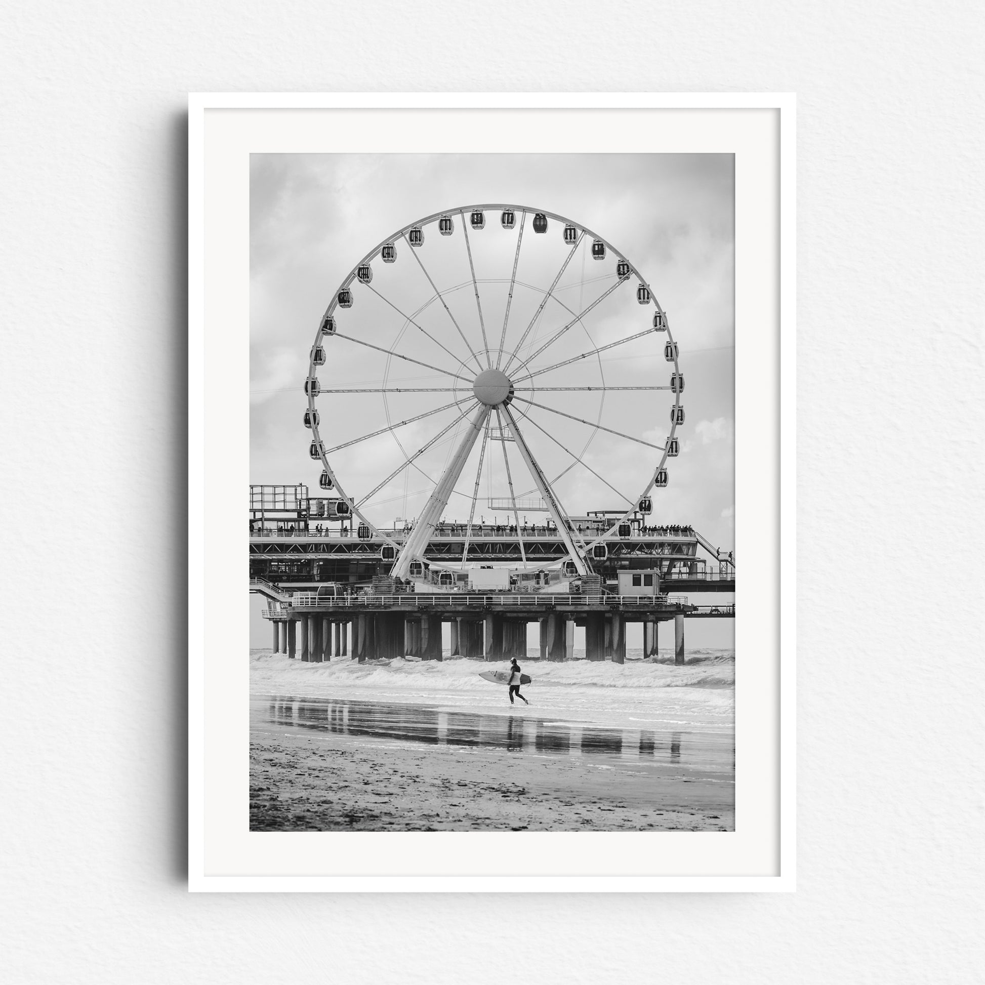 Black and white photograph of the iconic ferris wheel on Scheveningen Pier with a surfer, framed in white wood to enhance the photo’s contrast and detail.