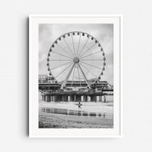 Load image into Gallery viewer, Black and white photograph of the iconic ferris wheel on Scheveningen Pier with a surfer, framed in white wood to enhance the photo’s contrast and detail.
